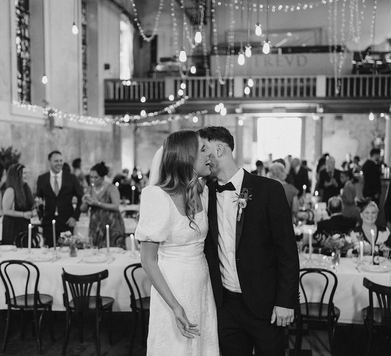 Groom in black tie kisses bride on the cheek at their wedding reception in Oxford 