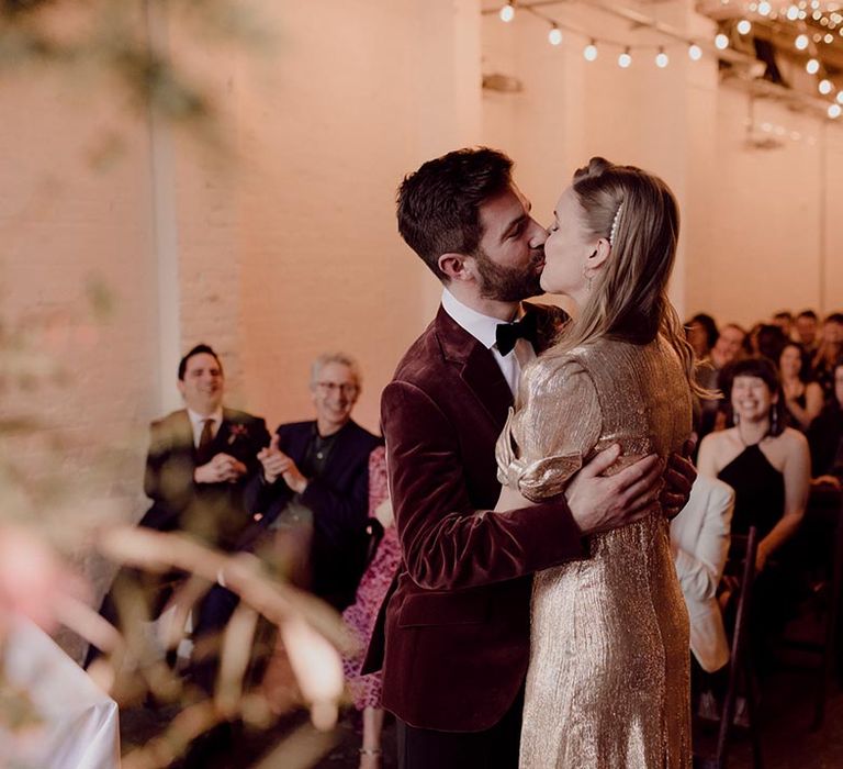 Bride and groom share their first kiss as a married couple in fairy lit industrial wedding venue, 100 Barrington 