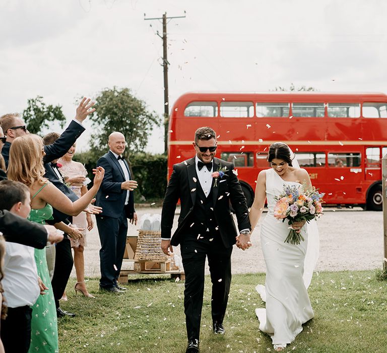 Bride and groom have confetti exit with red double decker bus wedding transport 