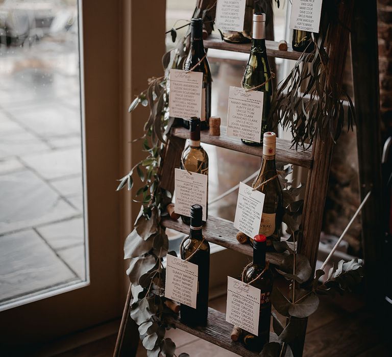 Wooden ladder seating chart finished with empty wine bottles and green foliage decor