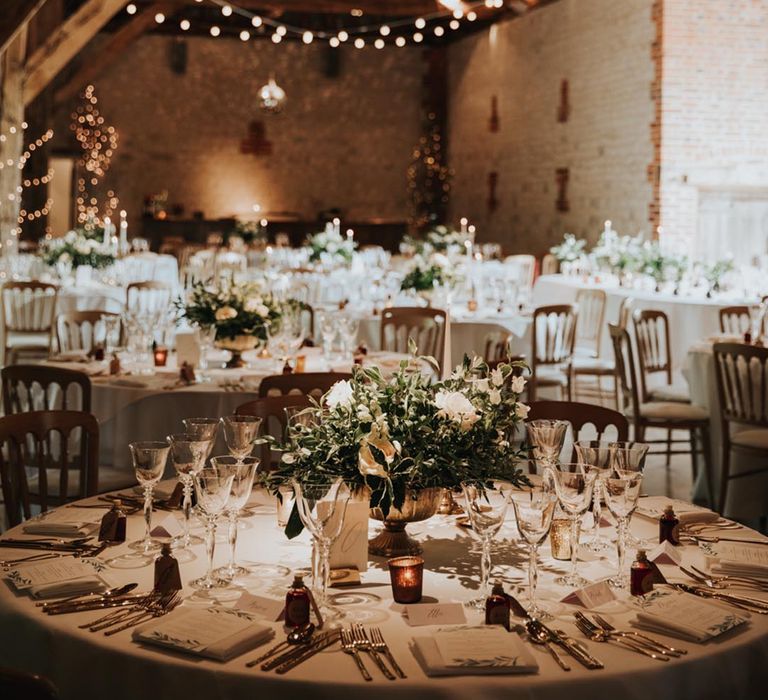 Dark neutral wedding tablescape at barn wedding venue reception room with fairy lights intertwined into wooden beams