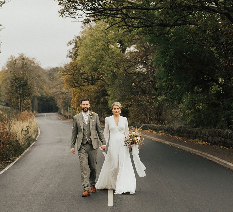 Bride in Reformation long sleeve wedding dress walks with her groom in three piece suit