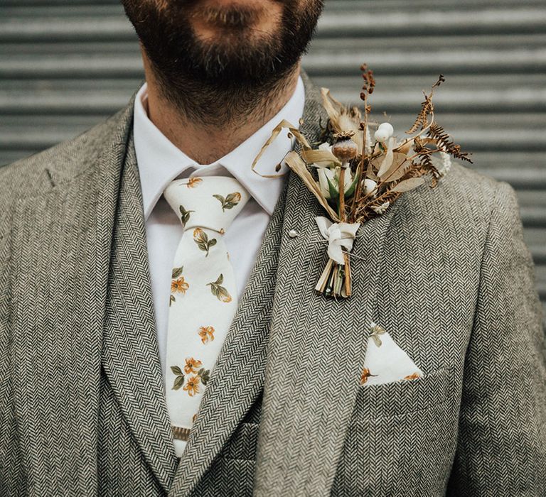 Groom wears dried floral buttonhole with white and floral styled pocket square and tie 