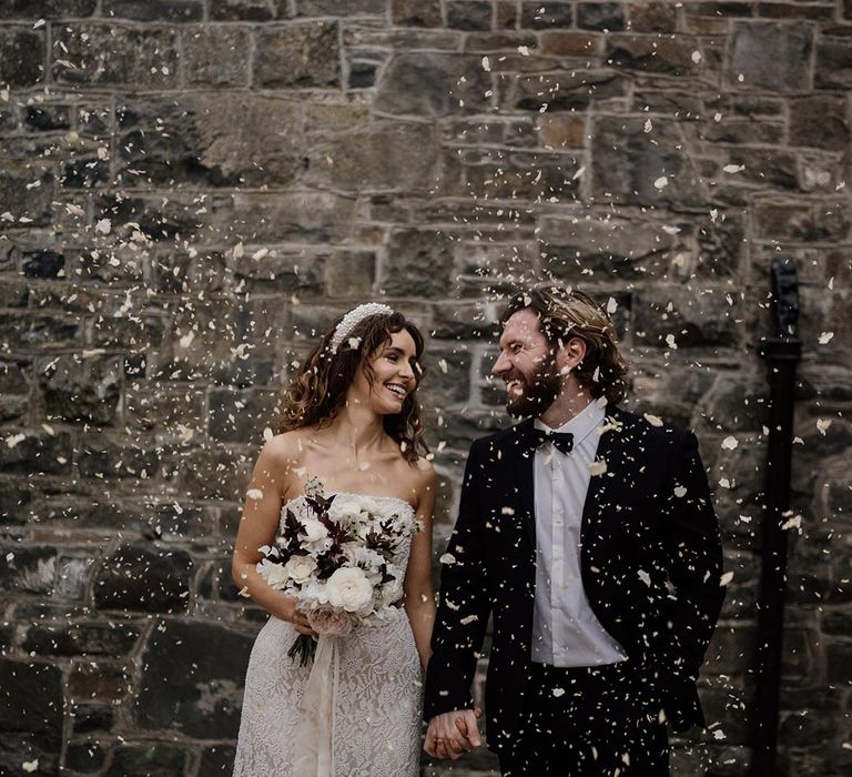 Bride in sleeveless lace detail wedding dress and groom in black tux exchanging looks