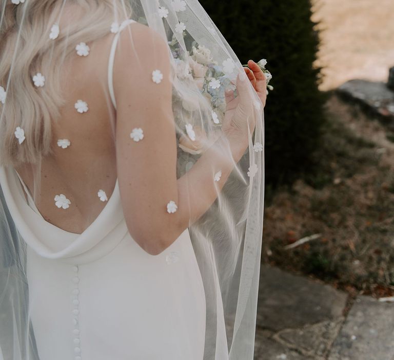 Bride in cowl back wedding dress with buttons wearing a flower applique veil 