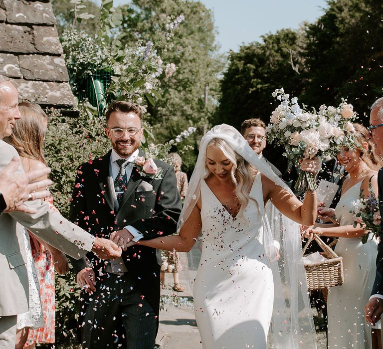 Groom in three piece suit with a large pink buttonhole with the bride in a Made With Love wedding dress have confetti moment 