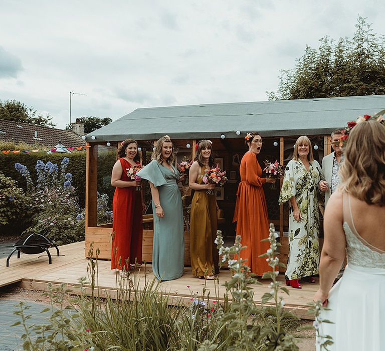 Bridesmaid smile as they get their first look at the bride all wearing mismatched bridesmaid dresses 