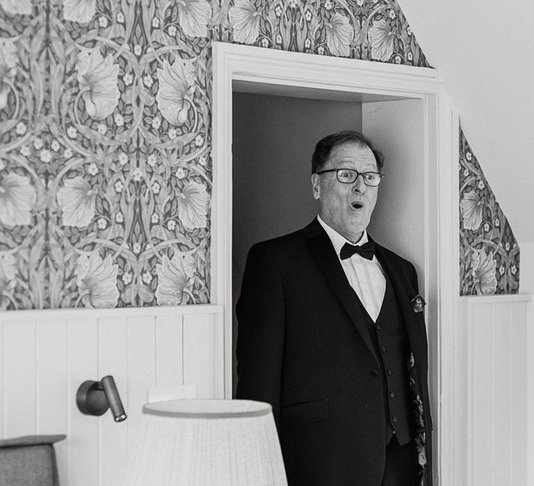 Father of the bride in black tie has a shocked facial expression as he sees the bride for the first time 