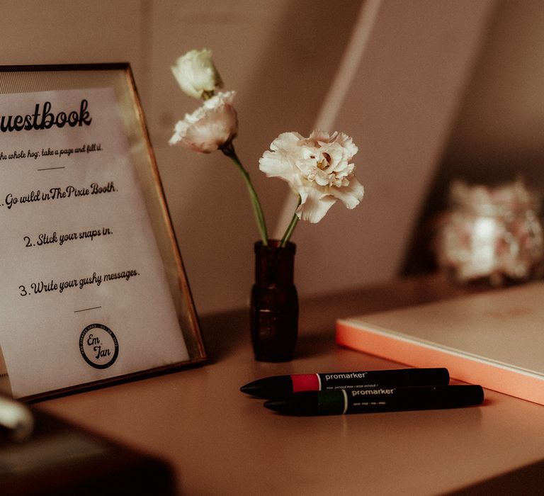 Retro style gold framed alternative wedding guestbook with small dark bottle with white carnations