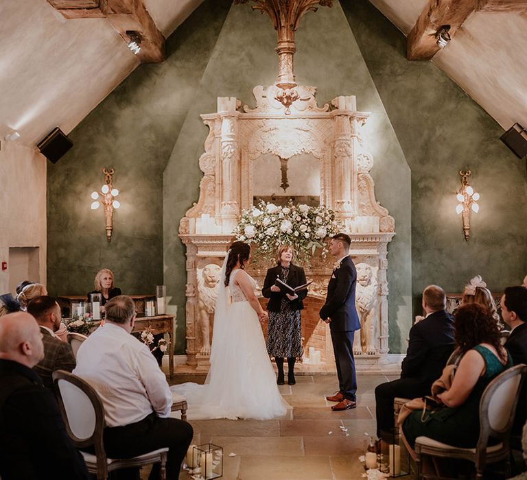 Bride & groom during wedding ceremony in front of extravagant fireplace 