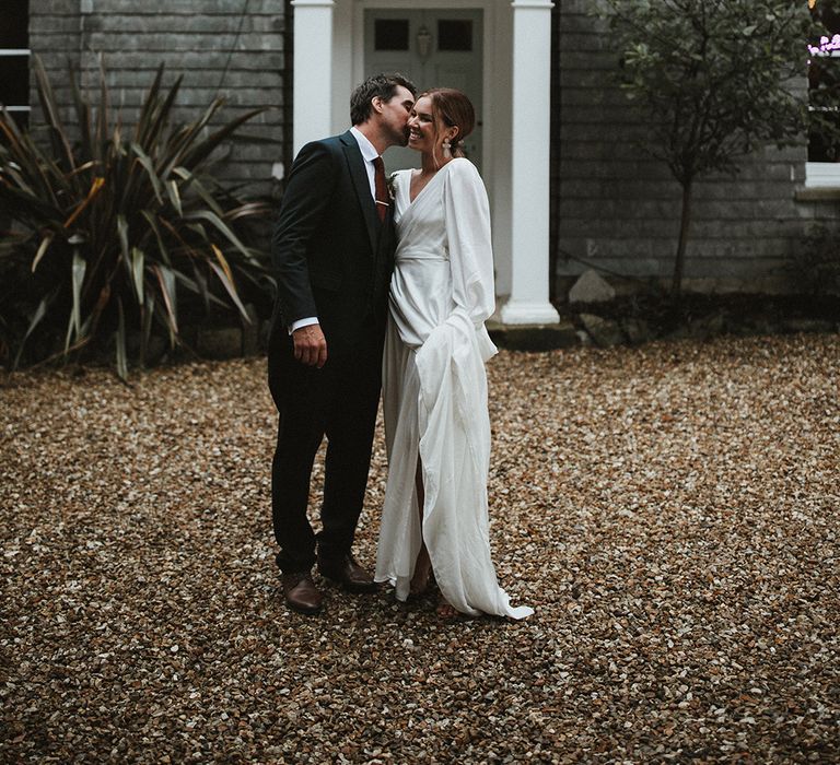 Bride wears floaty wedding dress by Aisla Munro complete with wrap styling and full sleeves as she stands beside her groom at Treseren