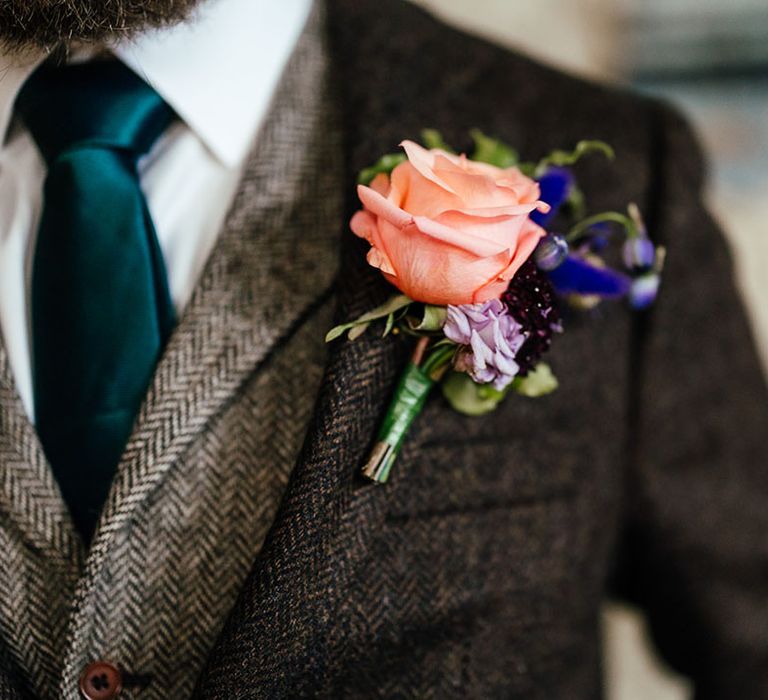 Groom wearing three piece wedding suit with deep green tie and pink garden rose, lilac carnation and purple flower boutonniere 