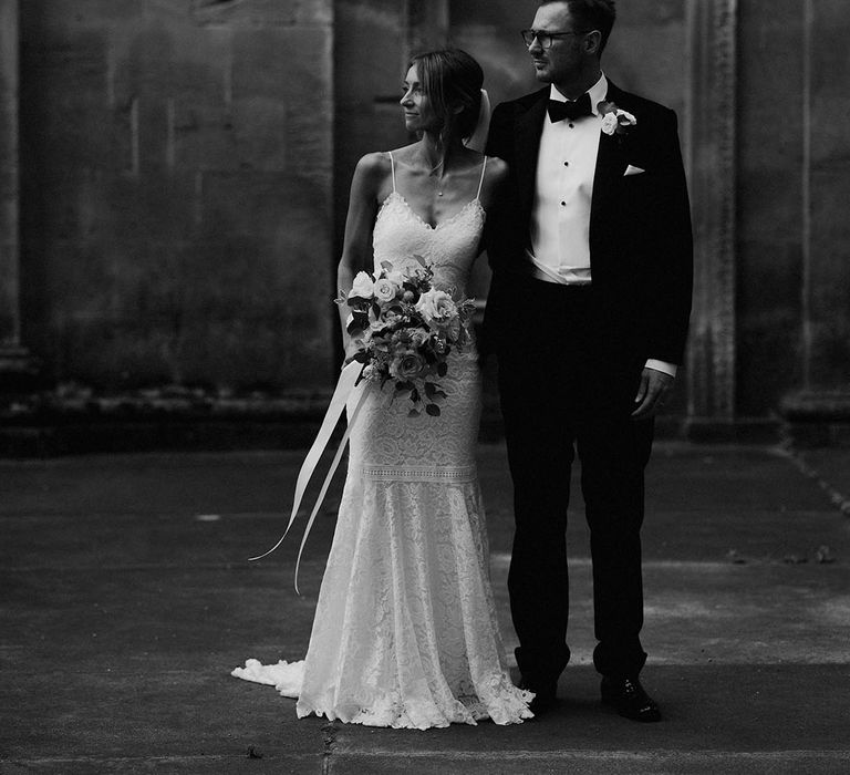 Groom in black tie with the bride in a Grace Loves Lace wedding dress walking together for their couple portraits 