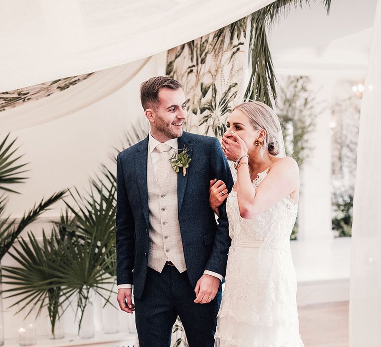 The bride in a lace wedding dress walks into the marquee reception with the groom and they both look so happy seeing the finished look 