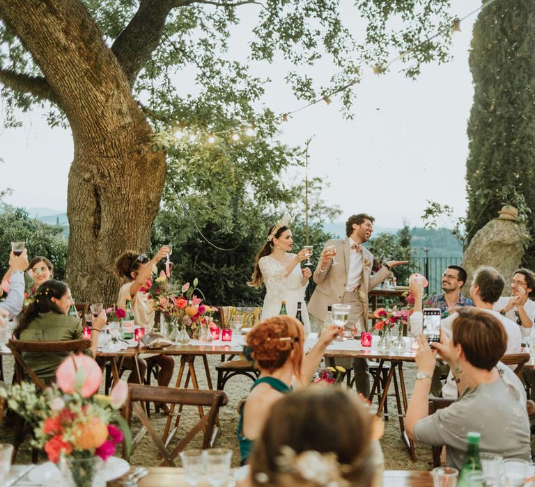 Bride and groom cheersing wedding guests at destination wedding breakfast in Italian hills.