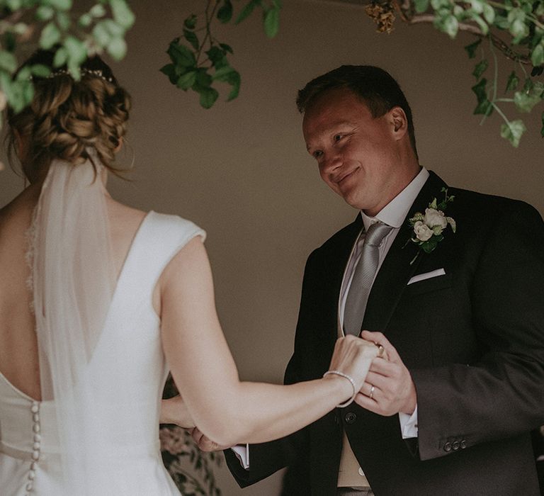 Groom in a navy suit with sage green tie smiles lovingly at the bride for their outdoor civil wedding ceremony at Hotel Endsleigh 