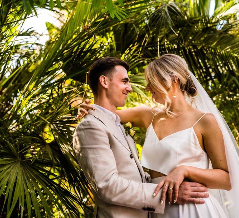 Groom in cream suit embraces the bride in a satin two piece bridal set for the relaxed and fun wedding at Sefton Park Palm House 