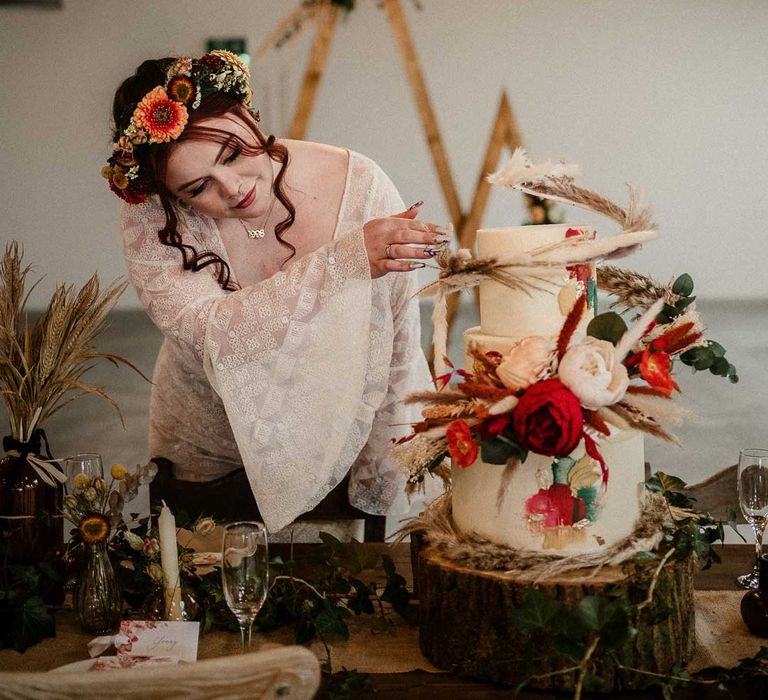 Bride wearing v-neck long bell sleeve boho wedding dress with boho rustic dried flower crown with a three tier buttercream wedding cake with large decorative pampas grass, eucalyptus, dried flower and garden rose cake topper on large tree stump cake stand at The Barn at Avington