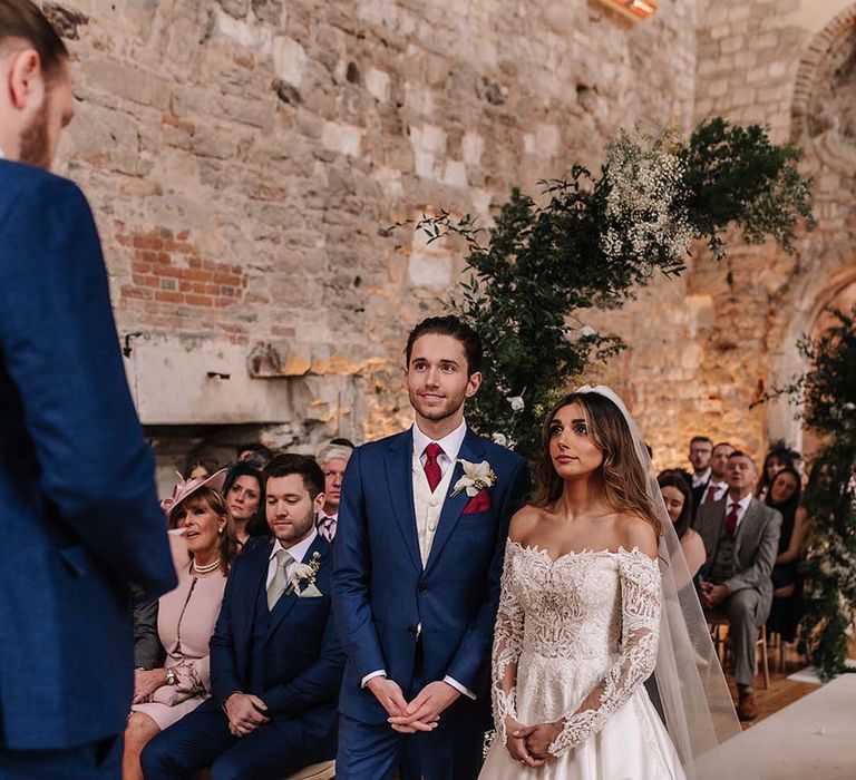 Bride in sparkly sequinned long sleeve wedding dress standing with the groom in a blue suit and red tie for their ceremony 