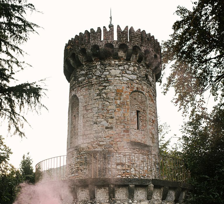 bride in a layered wedding dress kissing her groom whilst holding pink smoke bombs