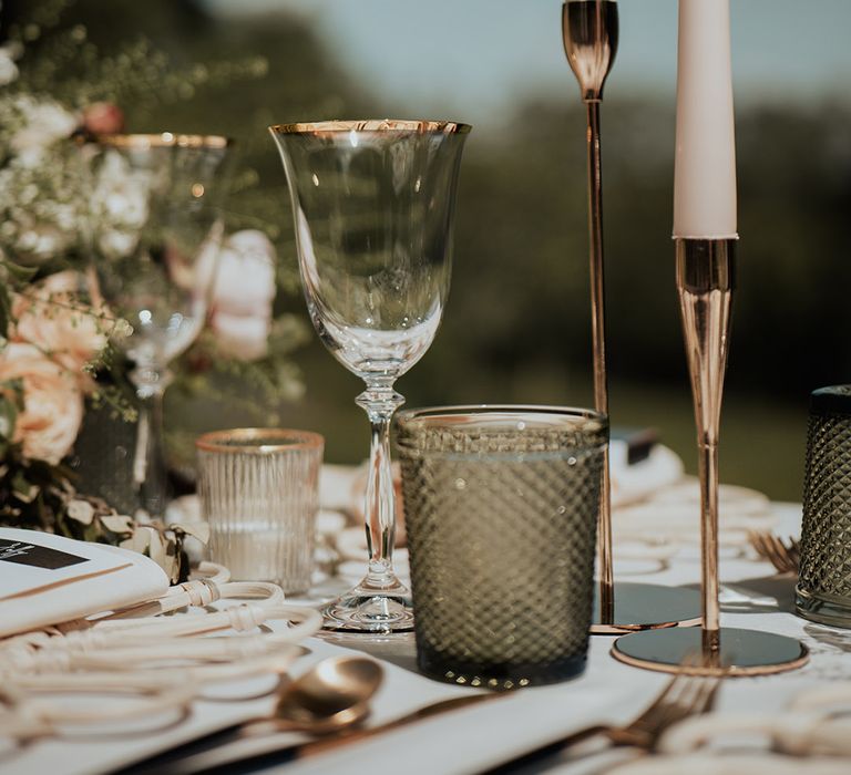 Gold rimmed glassware, gold candleholders with white taper candles and pink and white flower arrangements 