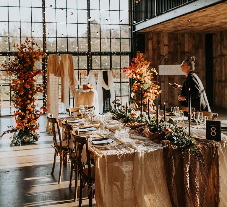 Hidden River Barn Carlisle wedding venue with autumnal tablescape decorated with drapery, autumn leaf flower columns, and black taper candles 