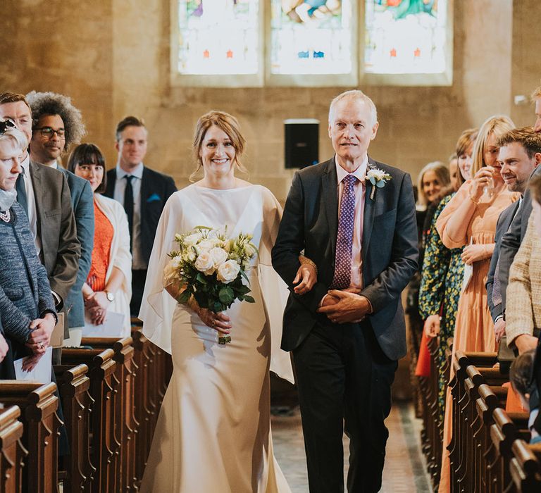 Father of the bride with pink shirt walking down the aisle with the bride at church wedding 