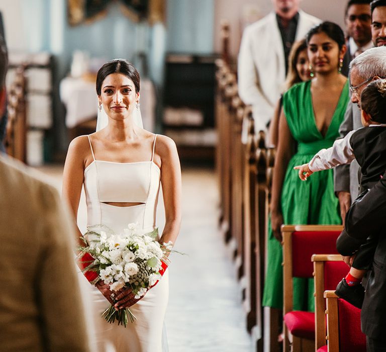 Bride in fitted slip wedding dress with cutout at the midriff walking to the groom down the aisle 