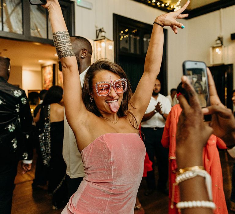 Wedding guest in pink dress with custom pink sunglasses dancing at the wedding reception 