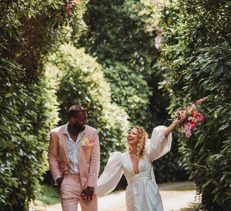 Bride in short wedding dress with puff sleeves walking with the groom in pink wedding suit and buttonhole 