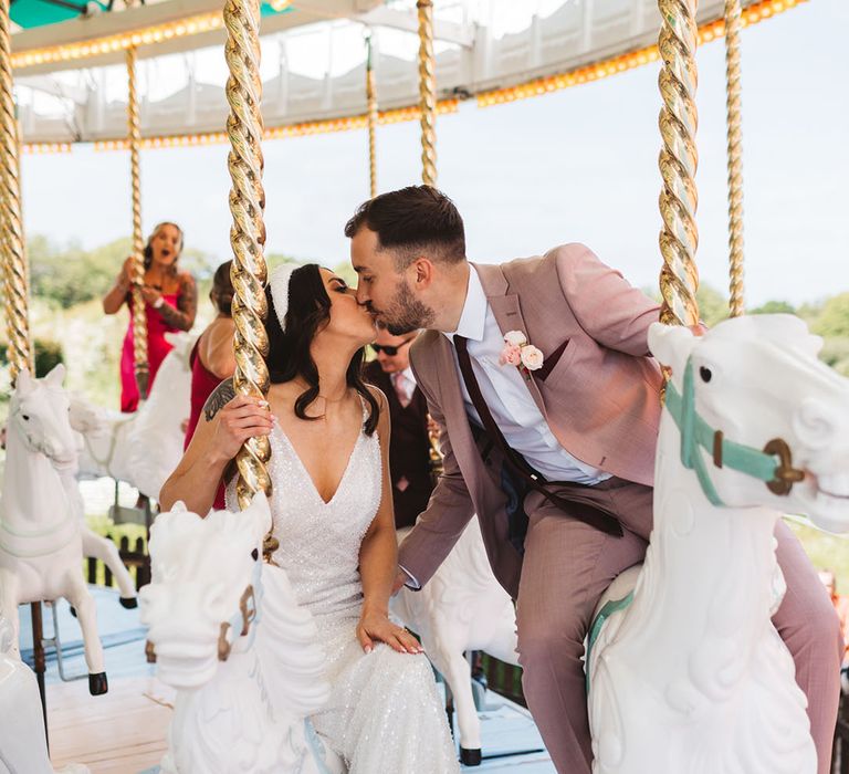 The bride in a sparkly wedding gown and metallic platform shoes with headband kissing groom on carousel at Preston Court 