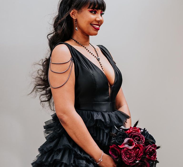 Bride in black ruffled wedding dress carrying red rose bouquet with black accessories 