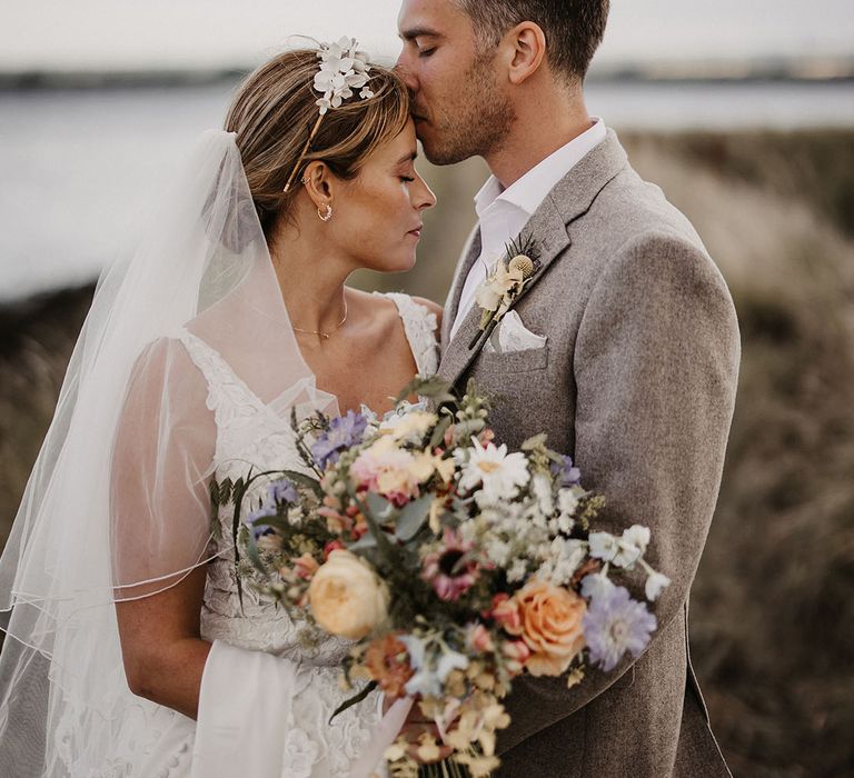 Bride holding pastel wedding bouquet with groom in beige stone suit 