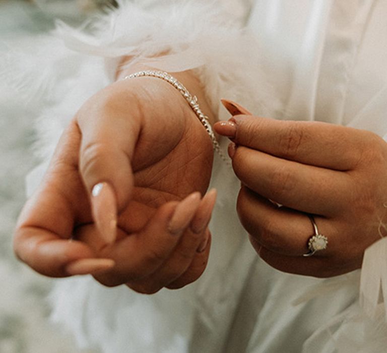 Bride with pointed almond bridal nails with neutral base colour with shiny top coat putting on silver bracelet 