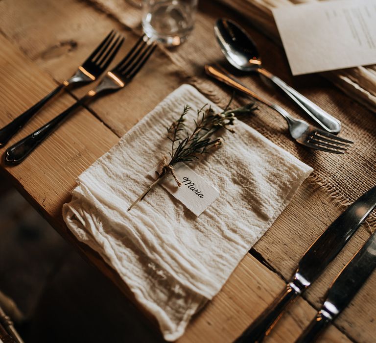 Rustic wedding place setting with white napkin, simple place name and sprig of flowers 