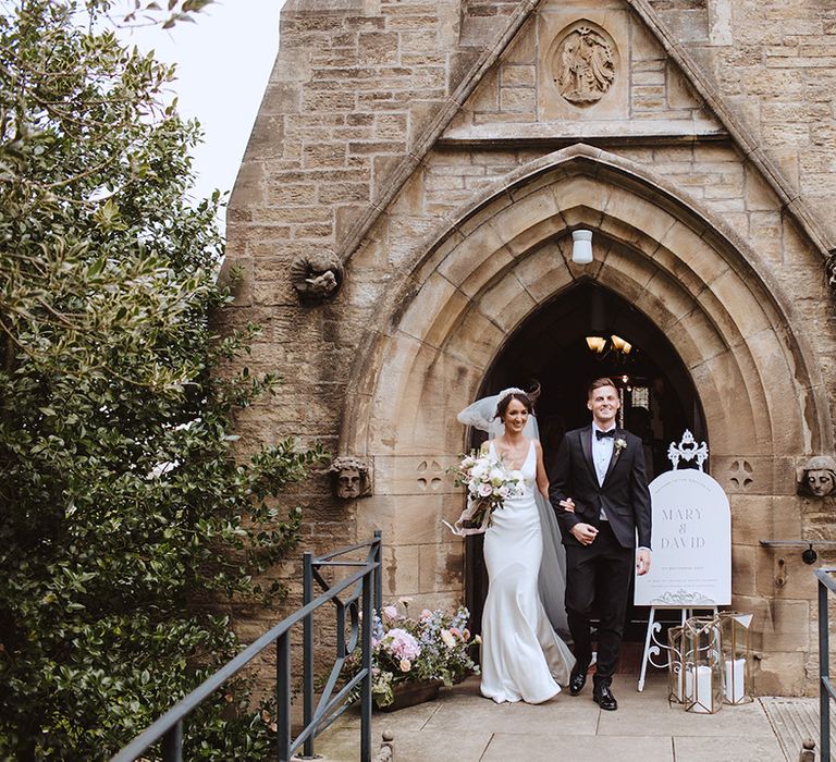 Black tie wedding dress code at church wedding with the groom in black tuxedo and bride in slip gown 