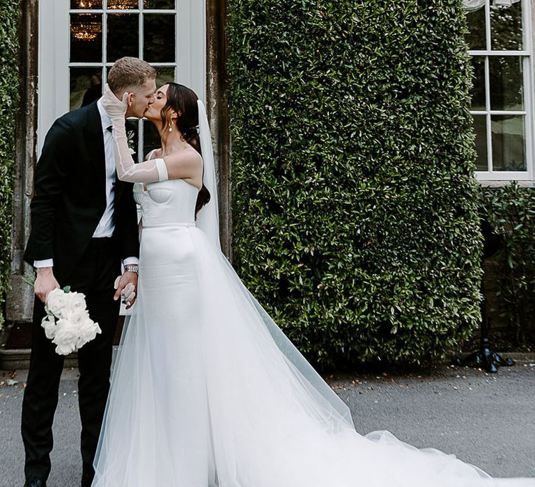 Bride kissing groom in black tuxedo at their classic and elegant luxe wedding 