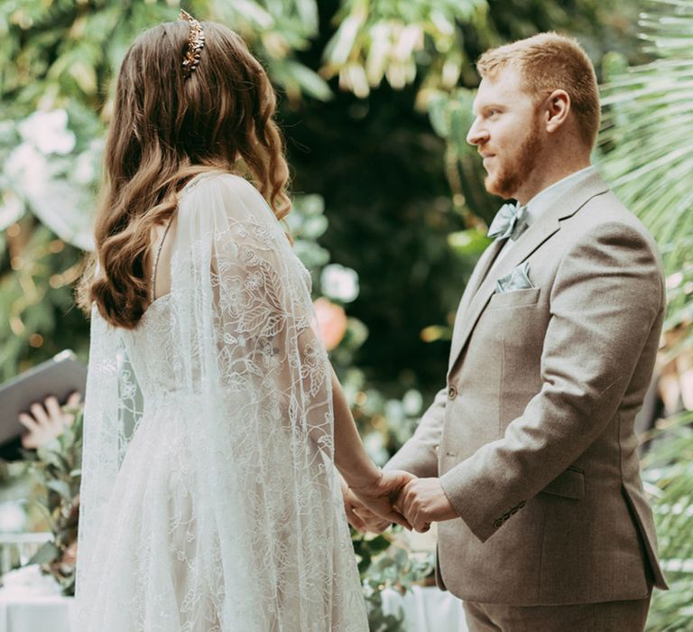 Bride and groom stand holding hands for their wedding ceremony at The Riverside Glass House wedding venue 