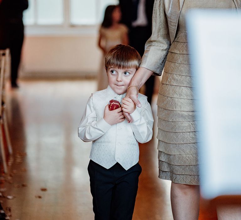 Page boy carries the wedding rings in a ring box as he is escorted up the aisle 