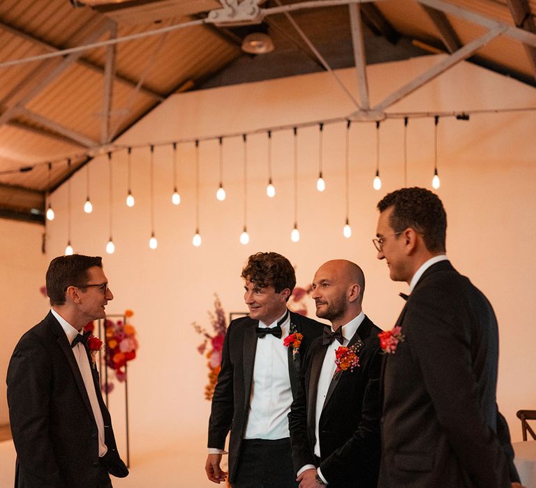 Groomsmen in black tuxedos with pink flower buttonholes 