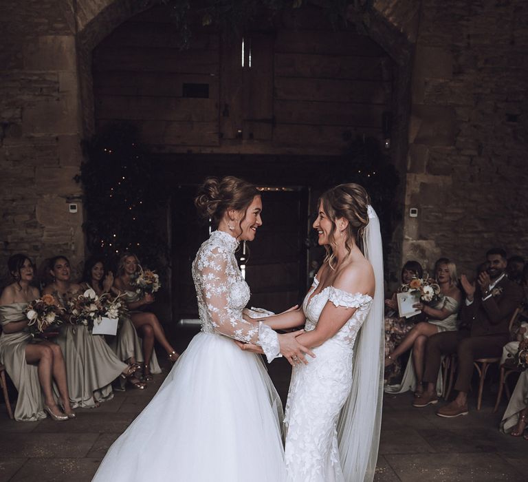 Brides at Stone Barn wedding in the Cotswolds holding hands for their wedding ceremony 