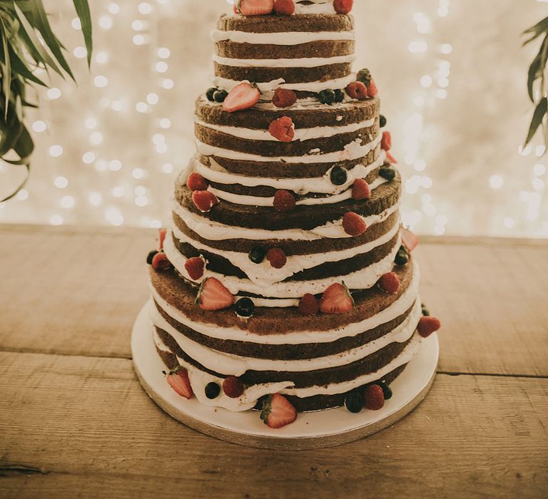 naked chocolate wedding cake with fairy light backdrop 