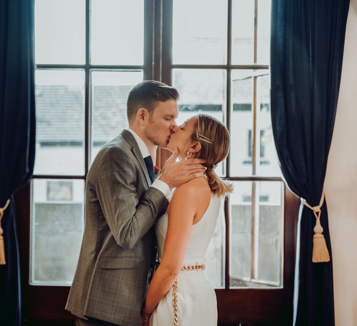 Groom kissing his bride in a Massimo Dutti jumpsuit for intimate micro wedding ceremony 