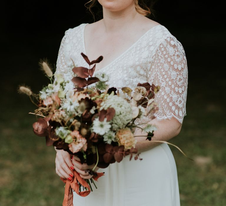 Bride holding her wild flower bouquet tied with ribbon 