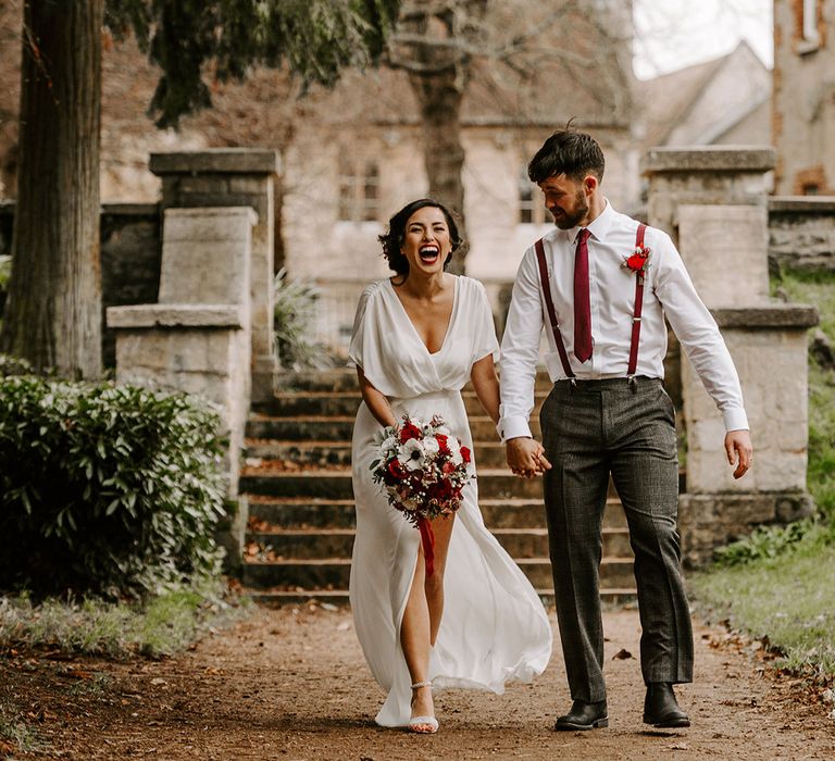 Laughing Bride and Groom in churchyard holding hands