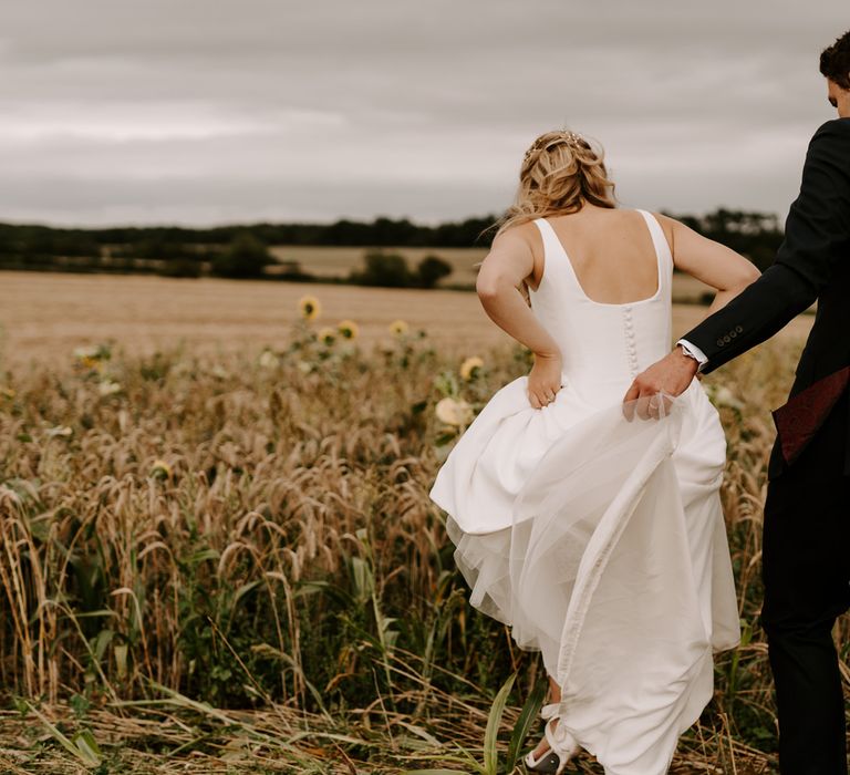 Groom holding up his brides dress with straps and button back detail 