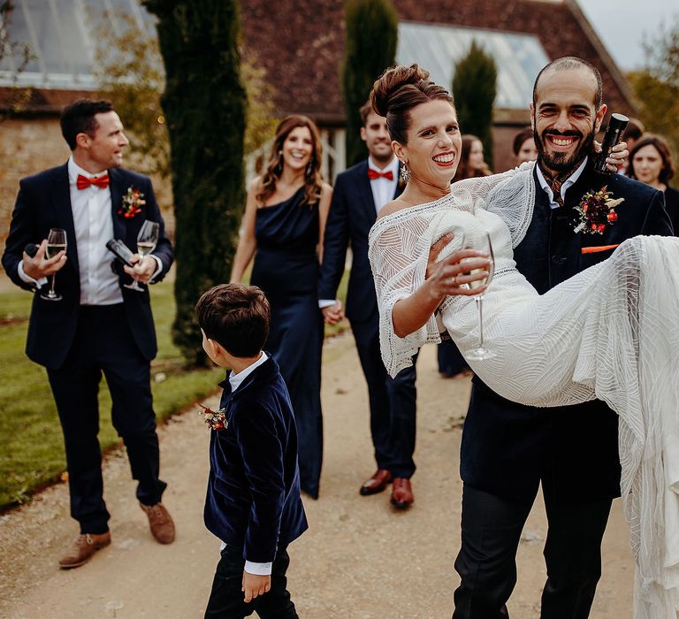 Groom carries bride through gardens after wedding ceremony