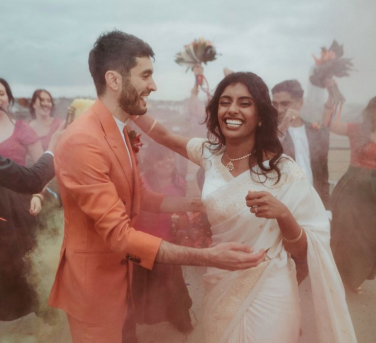 Smoke bomb wedding party portraits with groom in an orange suit and bride in a white sari 