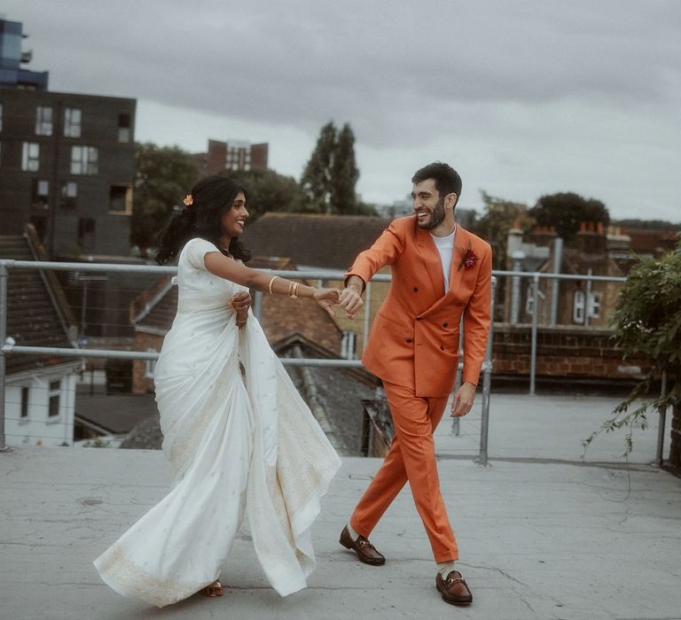 Portraits of a Sri Lankan bride in a white sari and Turkish groom in an orange suit on the roof at their wedding venue 