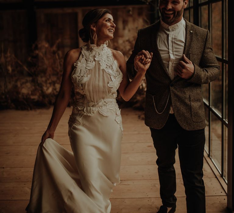 Groom in a grandad shirt and tweed blazer and bride in a halter neck wedding dress with lace detail and satin skirt